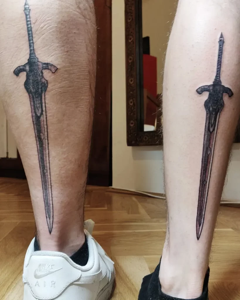 black and grey friendship tattoos on the back of the leg on 2 people. it's a sword from the game "dark souls".