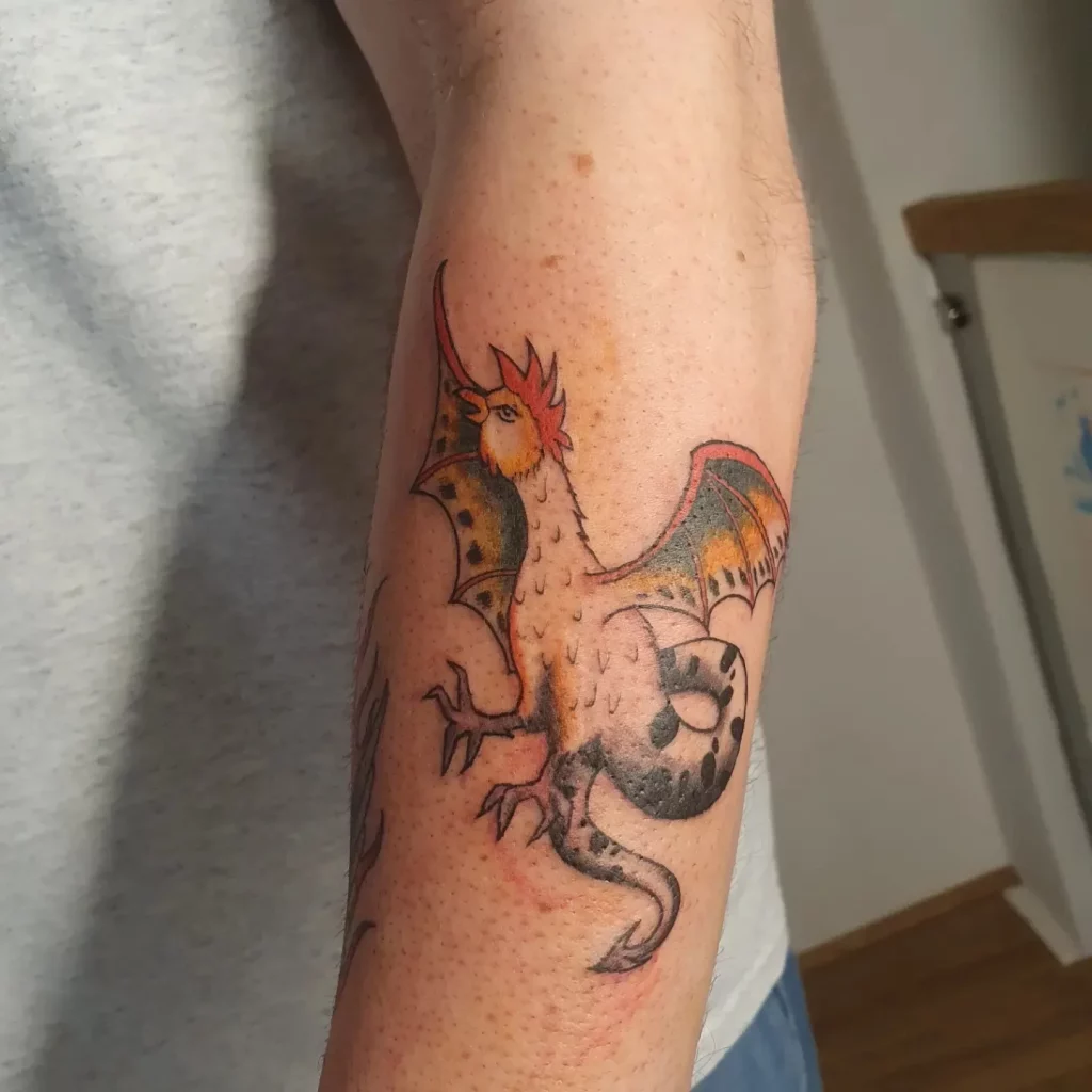 Tattoo on lower arm, a fineline basilisk in color