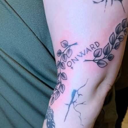 freehand lettering tattoo "onward", where the "o" is the feminine symbol. around it are some branches.