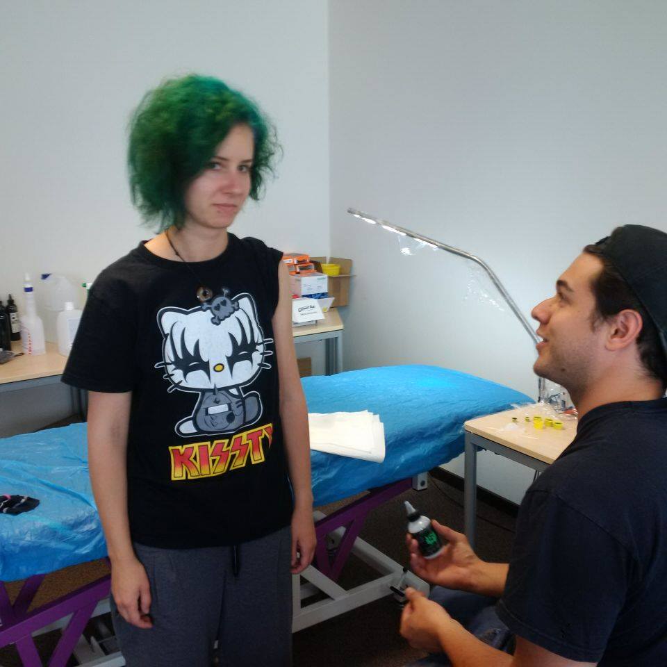 Lucy with green hair and a hello kitty-shirt getting prepared by her friend Bruno for her first tattoo in 2016.